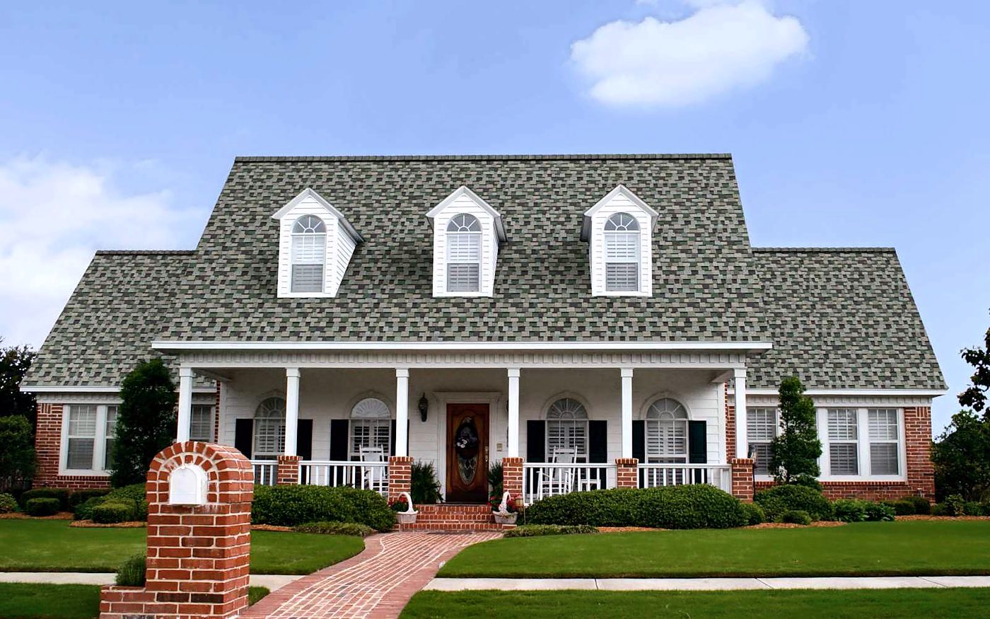 A white farmhouse with red brick accents roofed in Owens Corning TruDefinition Duration Designer shingles in Evergreen Mist