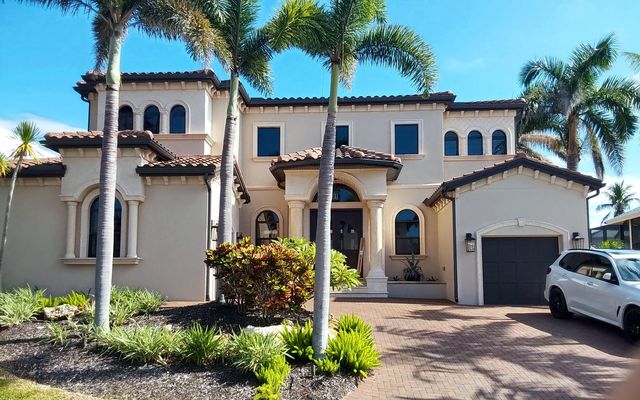 Two-story Mediterranean-style home with a concrete tile roof framed by palm trees