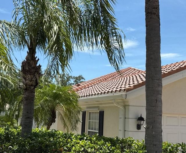 Single-story stucco home with a terracotta concrete tile roof behind palm trees