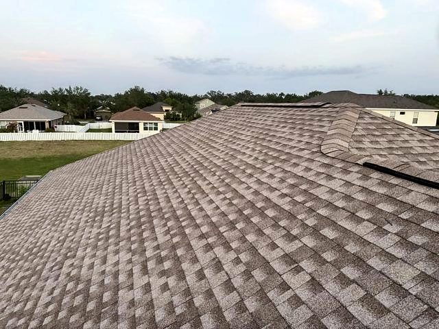 Wide brown-tan architectural shingle roof with a ridge vent at dusk