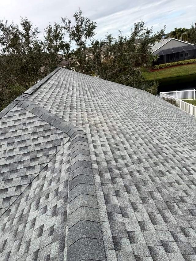 Gray architectural shingle roof hip with a ridge cap and trees beyond