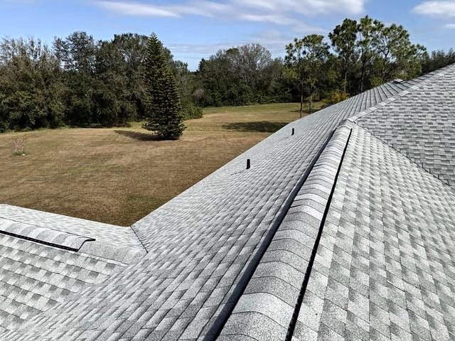Light gray shingle roof with ridge vents overlooking an open field