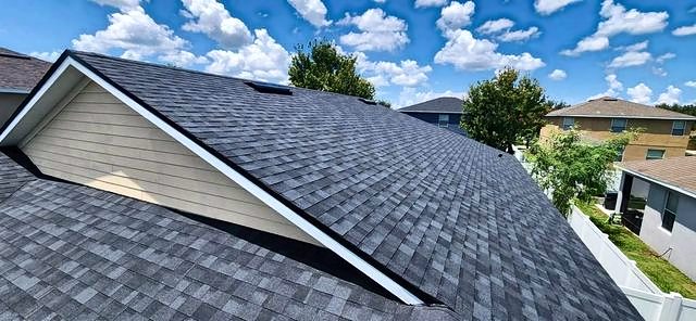Black architectural shingle roof with a white-trimmed gable against a cloudy blue sky