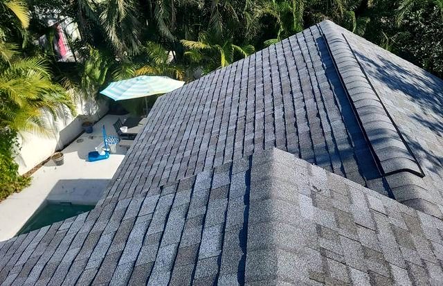 Gray shingle roof hip ridge above a pool deck with a striped umbrella