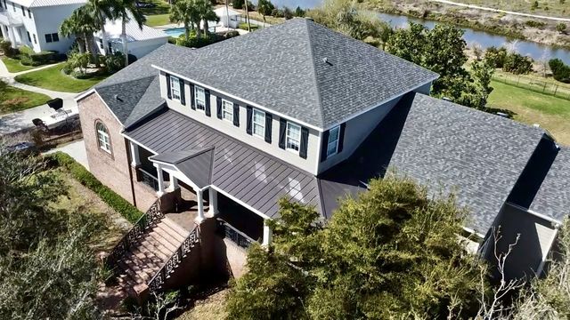 Aerial view of a two-story home with a gray shingle main roof and a dark standing seam metal lower roof
